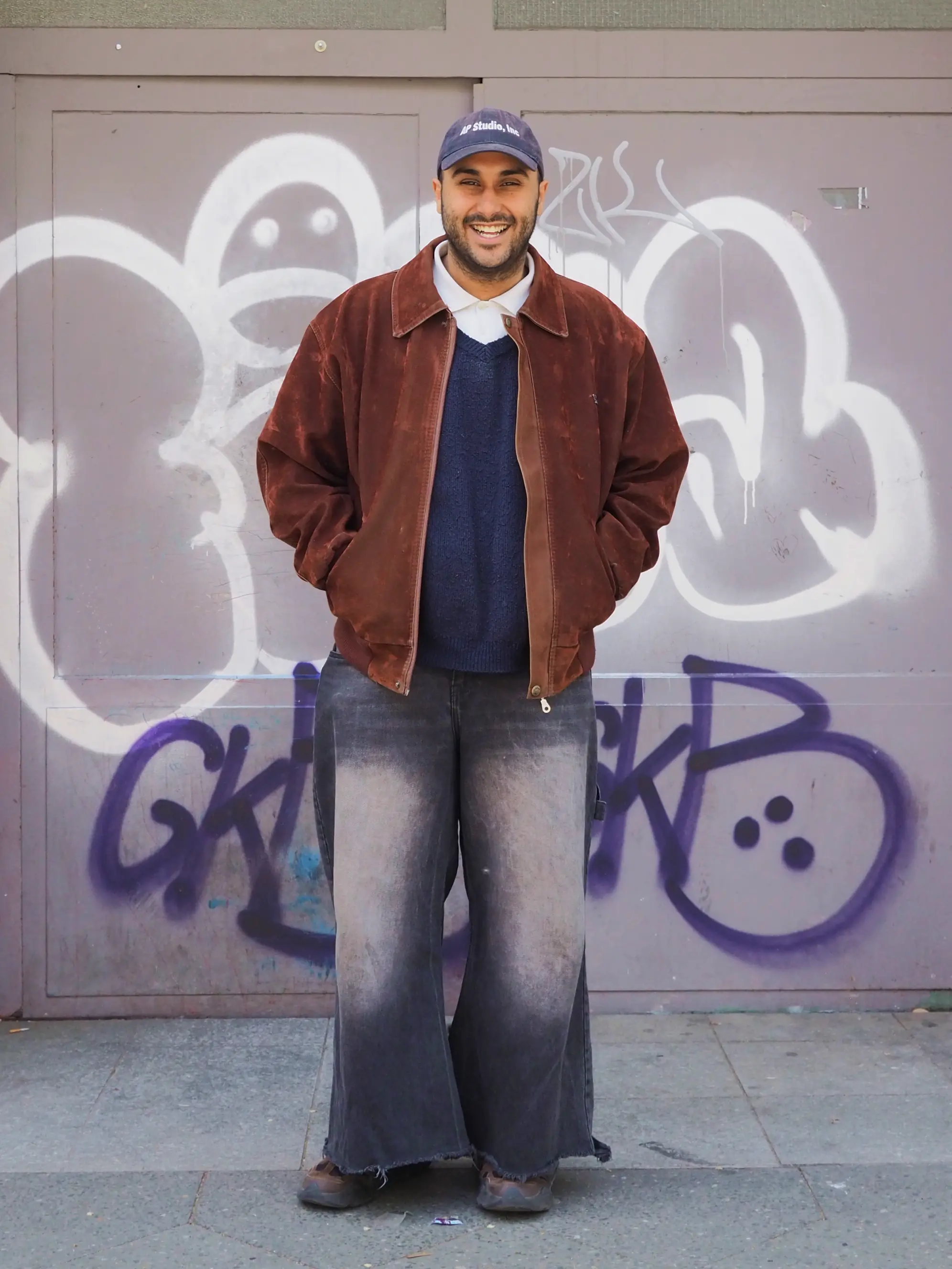 Junger Mann mit Schlaghose und Wildlederjacke vor Grafitti