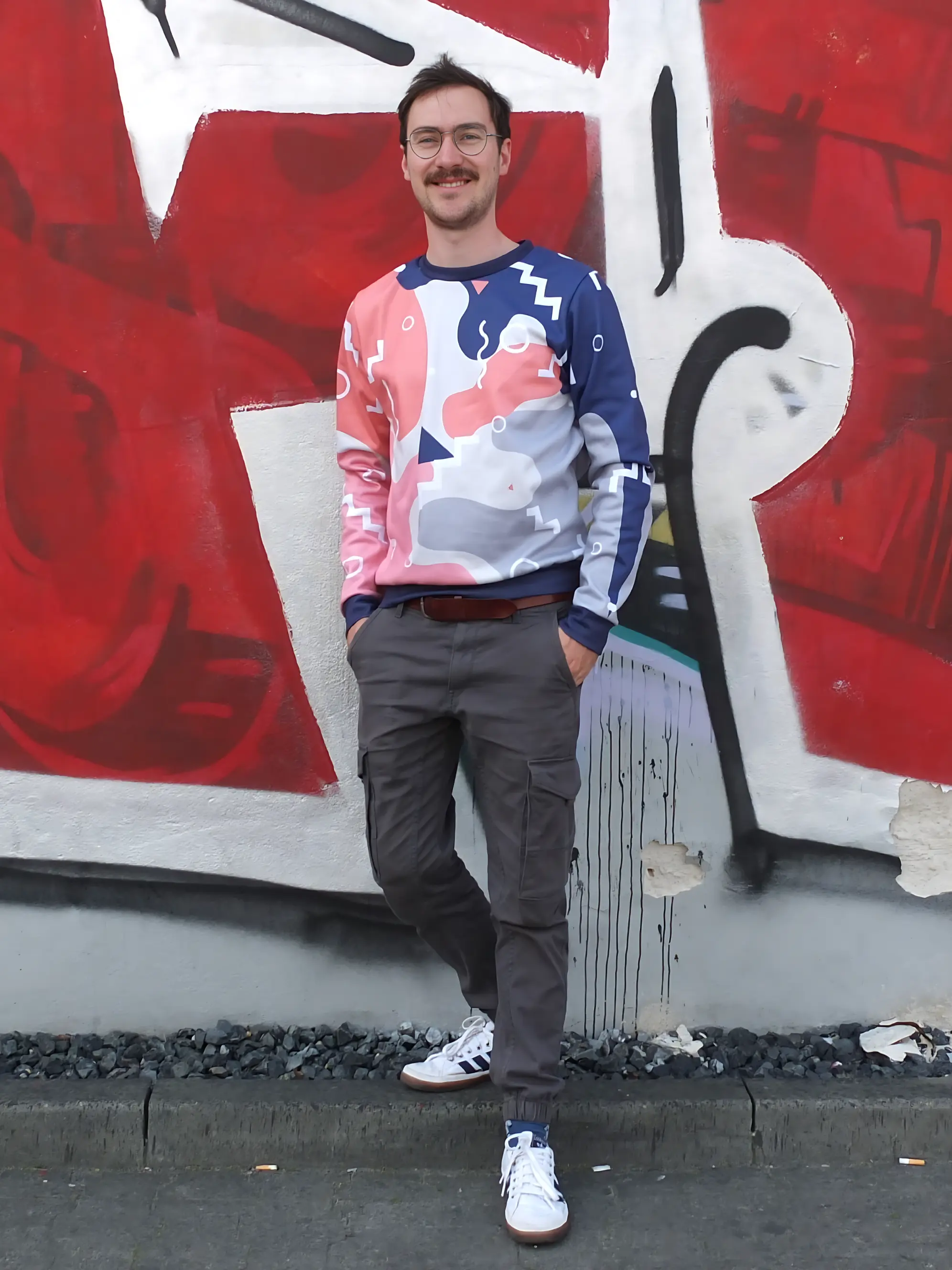 Junger Mann mit buntem Pullover vor Grafitti