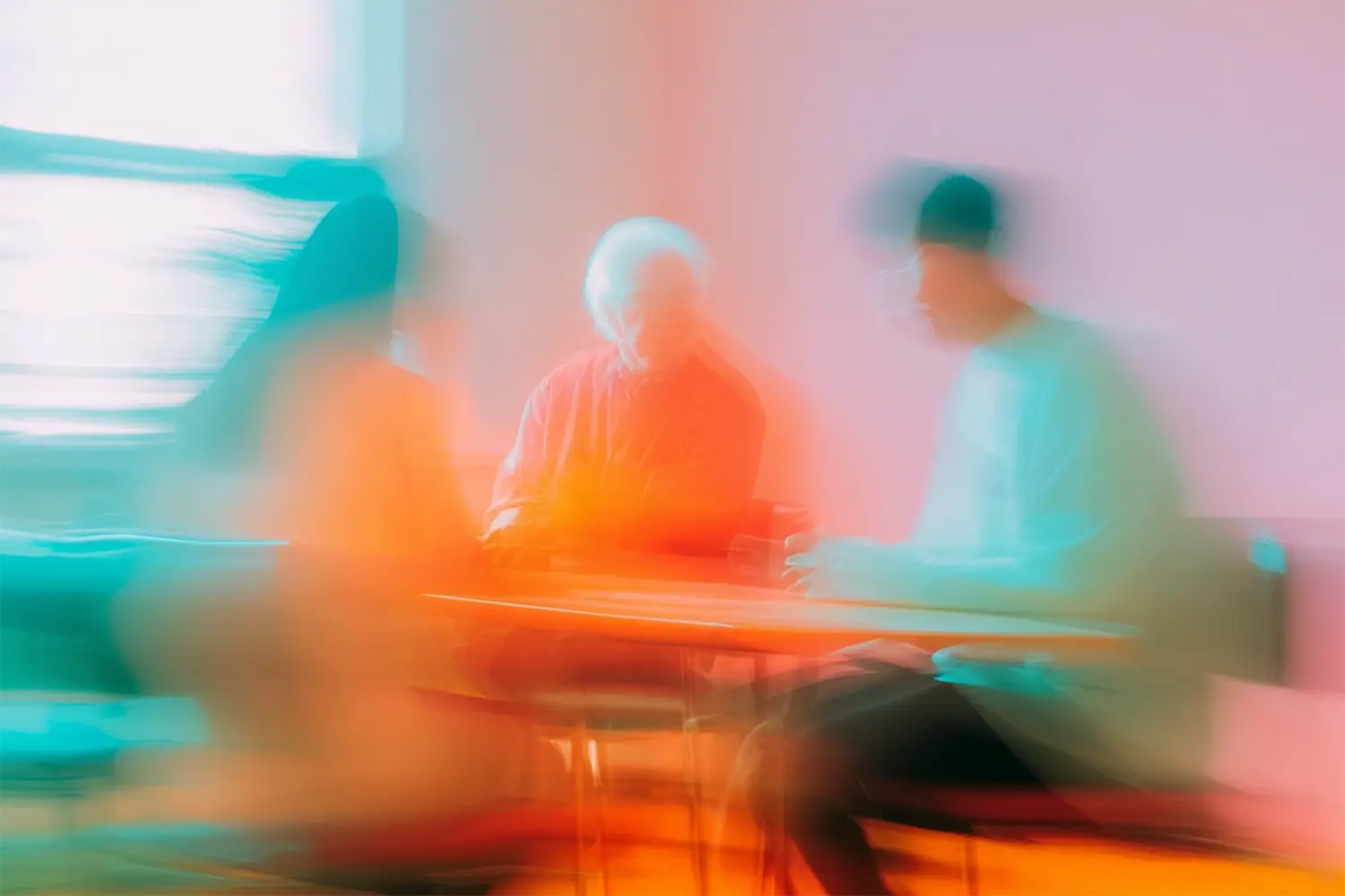 Drei stilisierte, verwischt dargestellte Personen sitzen an einem Tisch. Eine von ihnen ist alt (weiße Haare), zwei sind jünger. Drei stilisierte, verwischt dargestellte Personen sitzen an einem Tisch. Eine von ihnen ist alt (weiße Haare), zwei sind jünger.