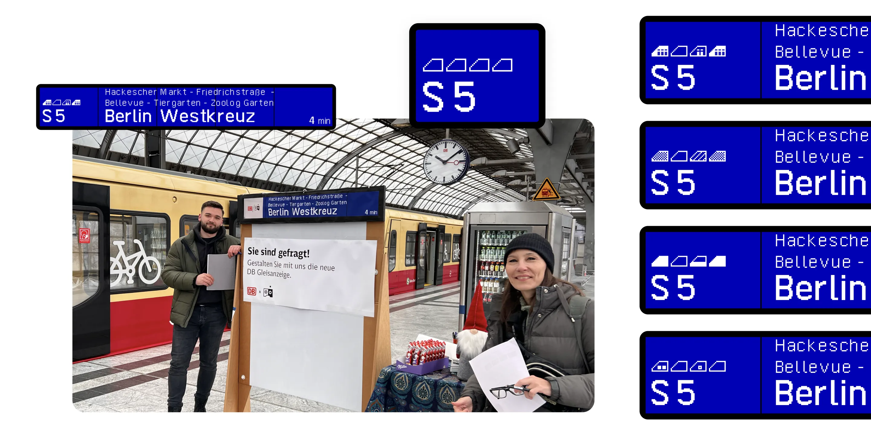 Two people stand on a train platform, one holding a sign, with a train in the background.