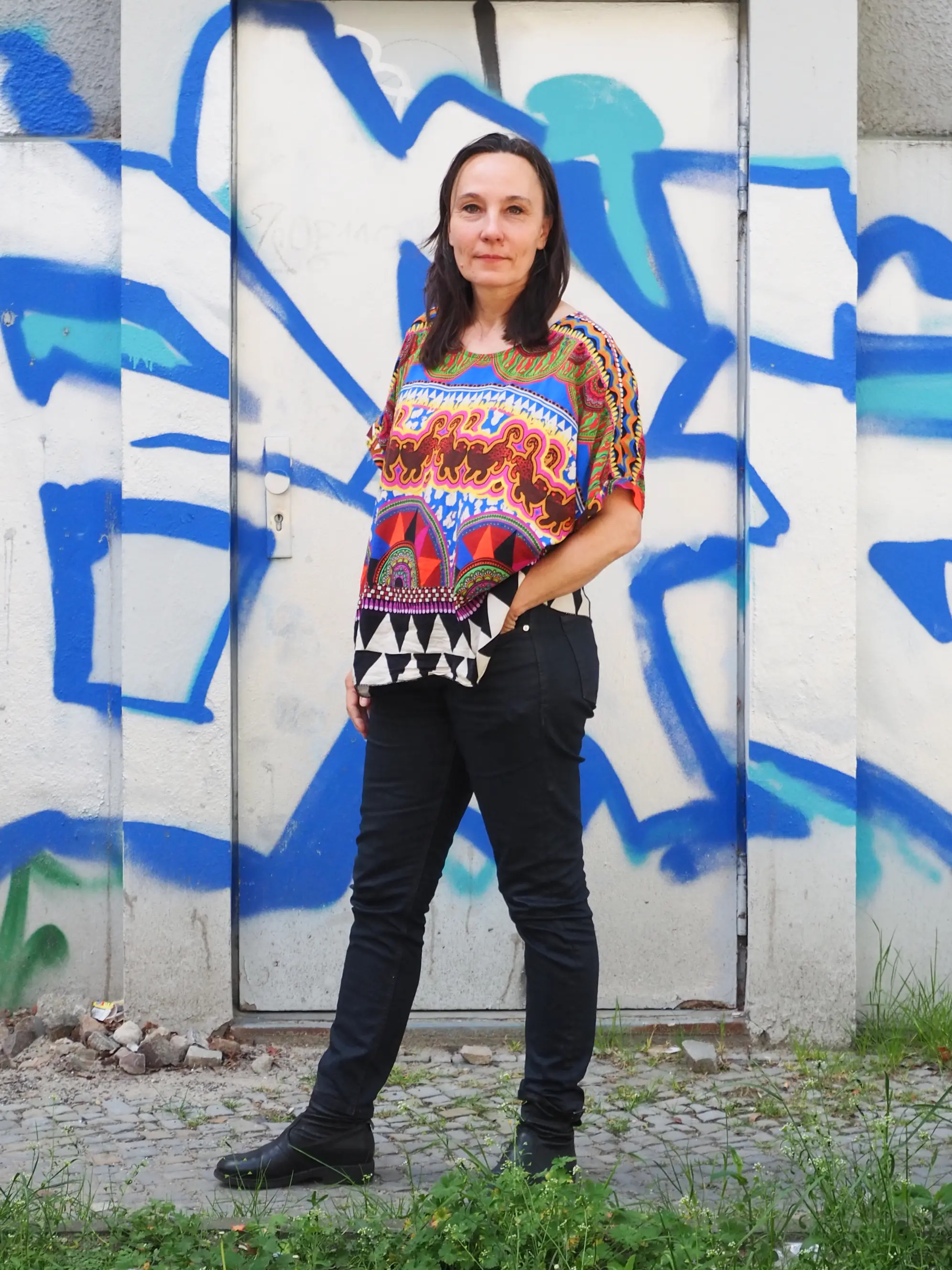 Junge Frau mit schwarzer Hose und buntem Oberteil vor Grafitti