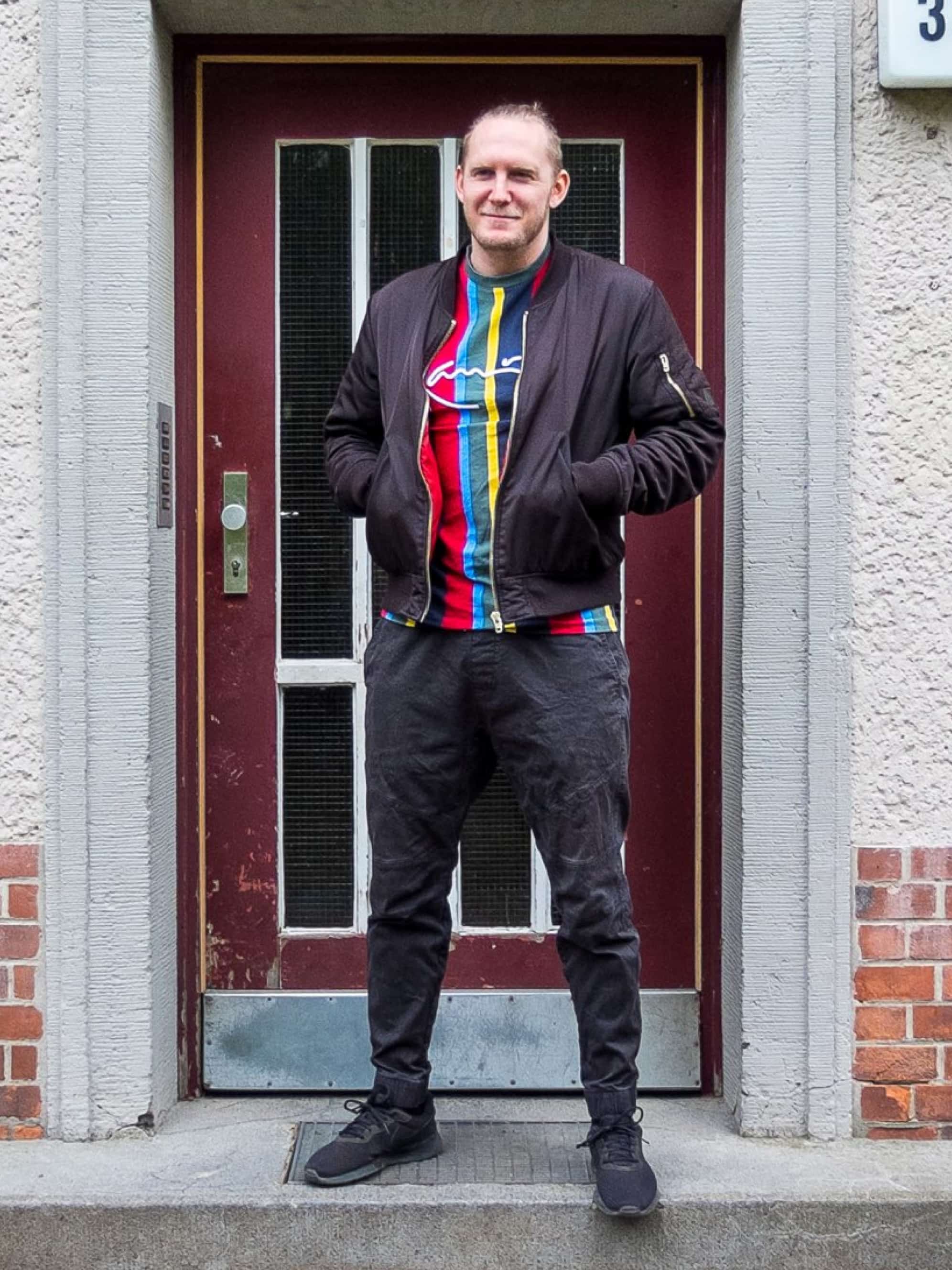 A man in a colorful sweater stands in front of a front door.