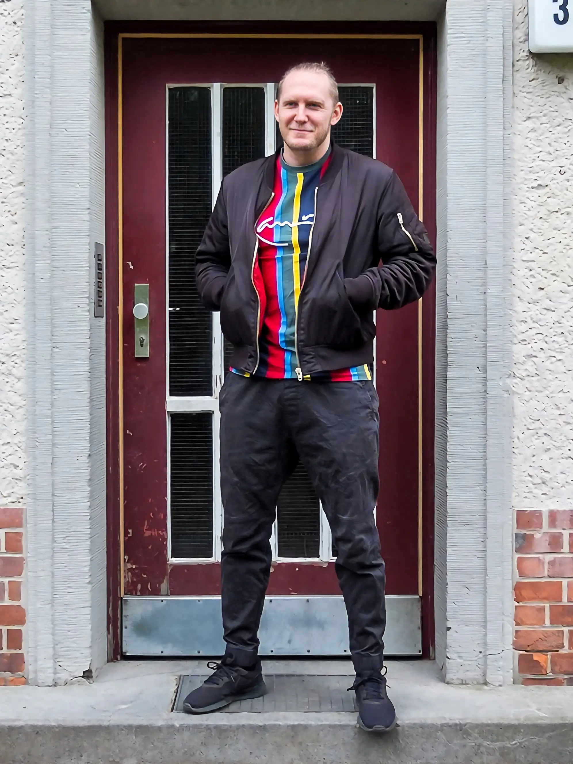 Schwar gekleideter Mann in Gewinnerpose vor Hauseingang