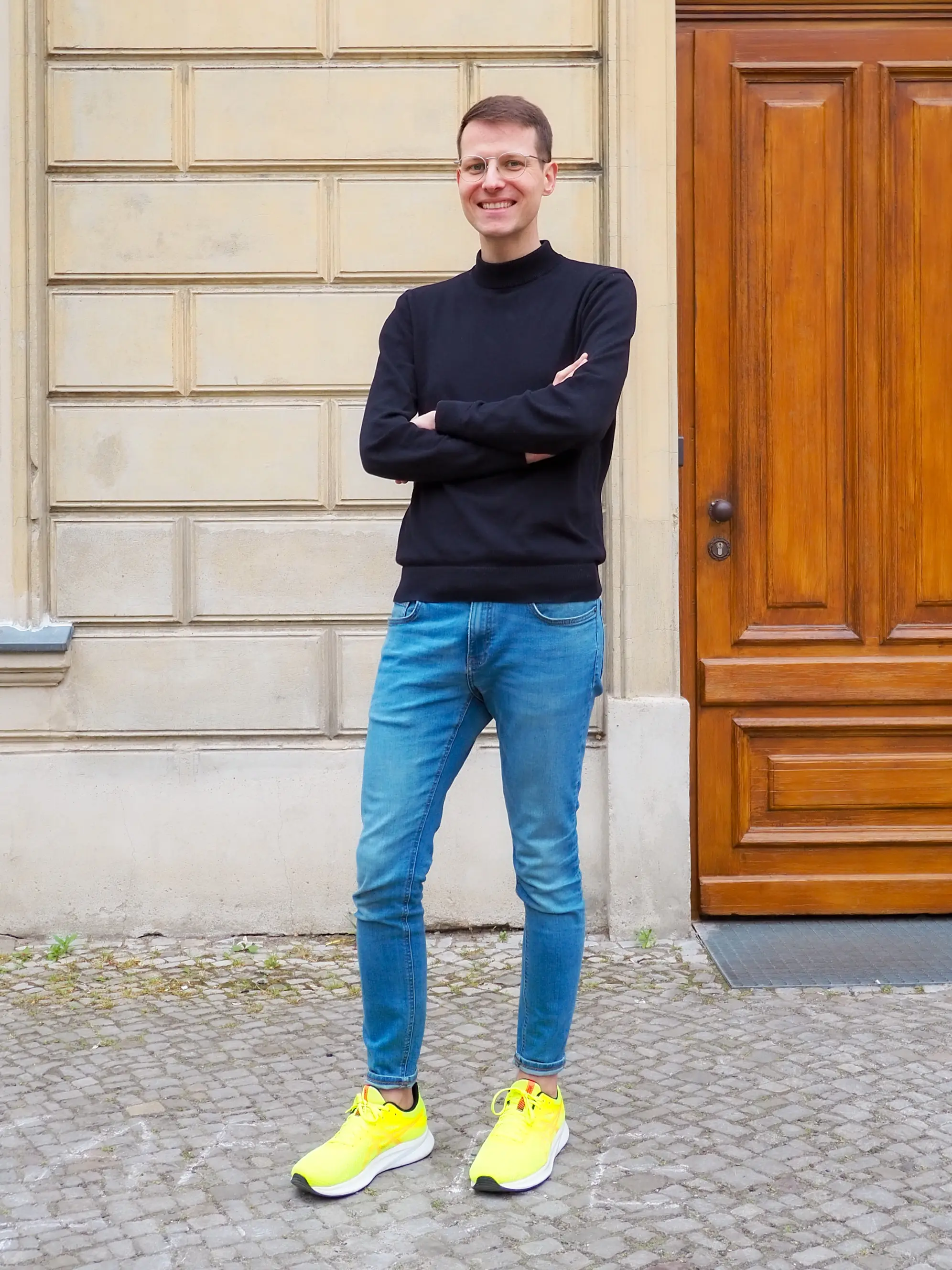 Mann mit Blue Jeans, gelben Tunrschuhen und dunkelblauem Sweater vor Hauseingang