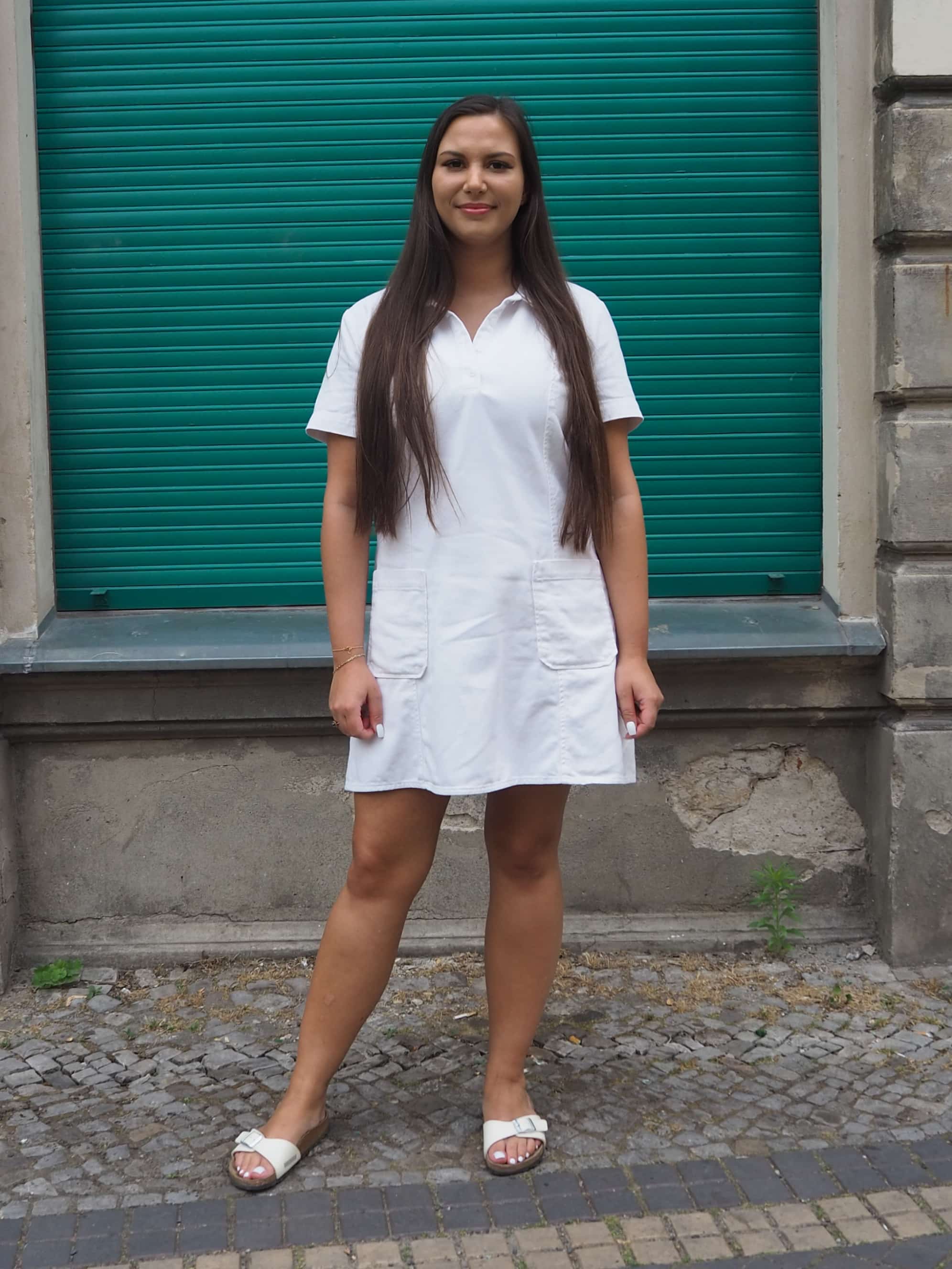 Eine Frau in einem weißen Kleid steht auf einer Ziegelmauer.