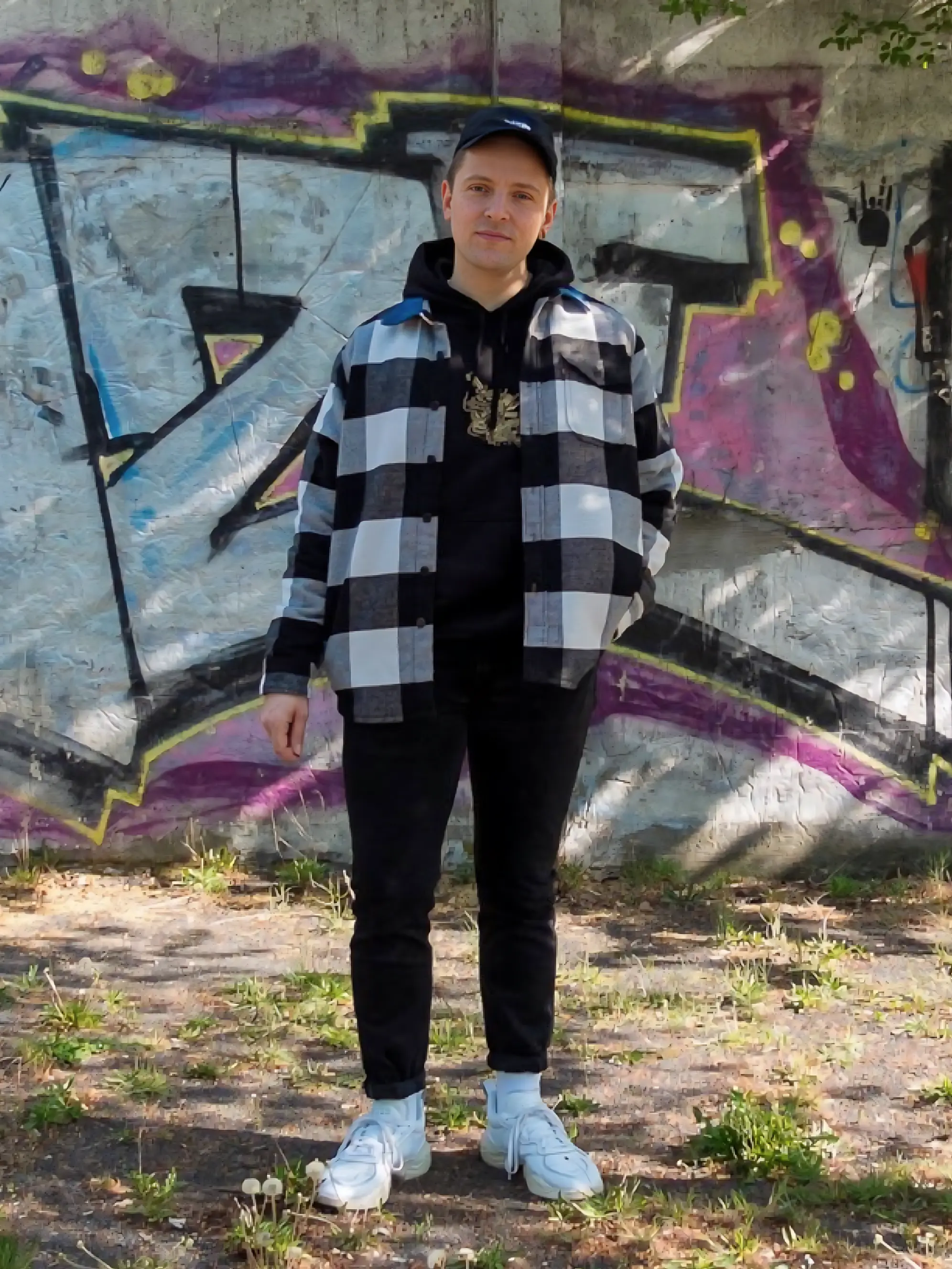 Mann mit karierter Jacke und Cap vor Grafitti