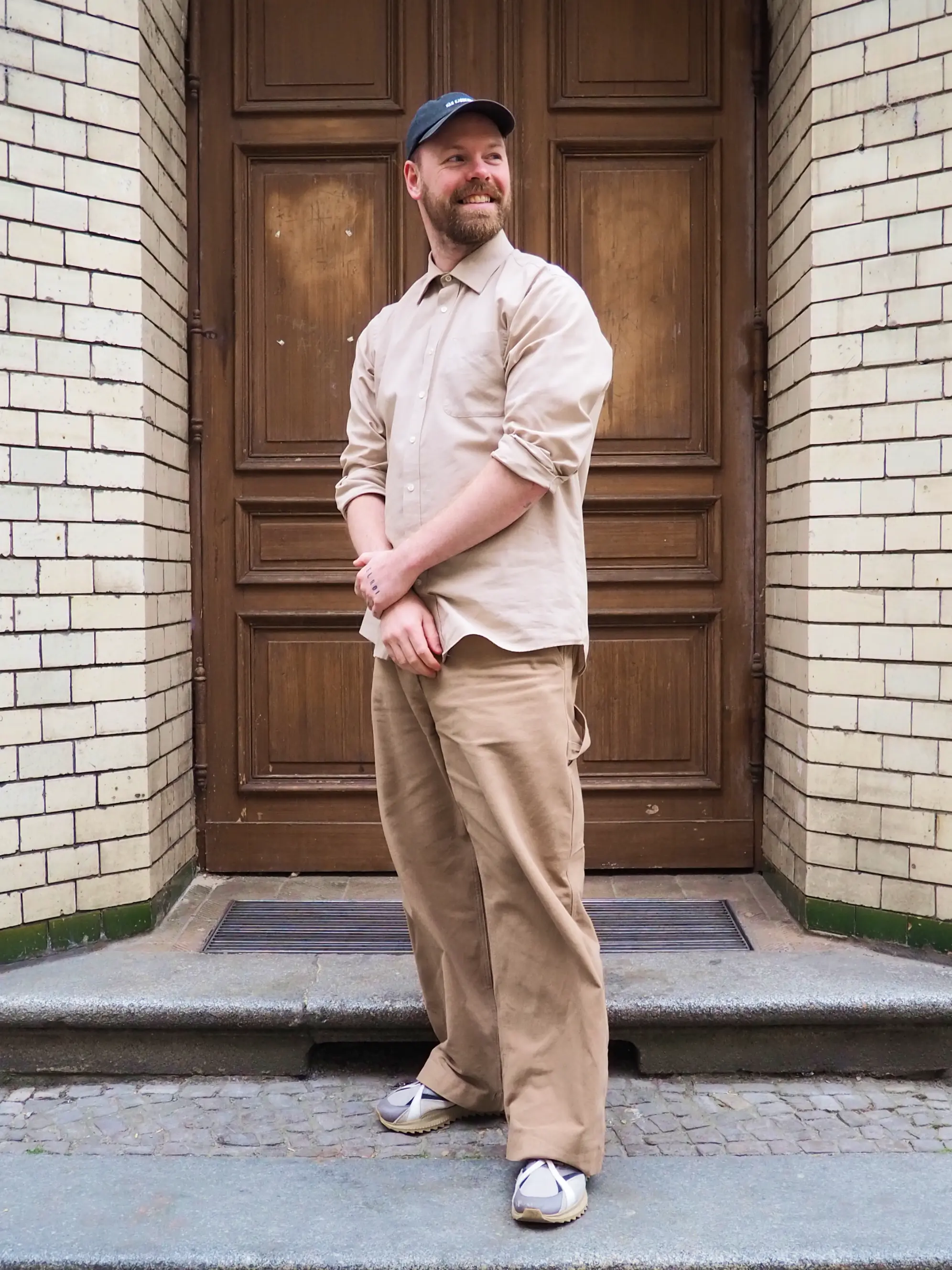 Mann mit beiger Hose und beigem Oberteil vor beige gekacheltem Hauseingang